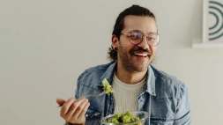 Jonge man met bril eet een groene salade aan tafel