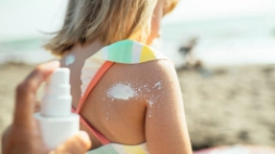 iemand smeert zonnecrème op rug van kind op het strand