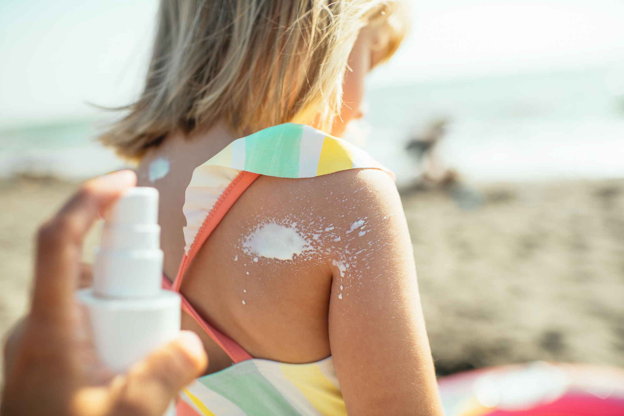 iemand smeert zonnecrème op rug van kind op het strand